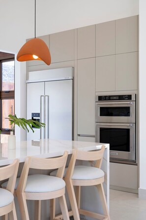 Una cocina moderna con un refrigerador blanco, horno doble y una mesa de comedor de madera con sillas.