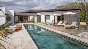 Ein modernes Haus mit Swimmingpool, Sitzgelegenheiten im Freien und einer Steinmauer.