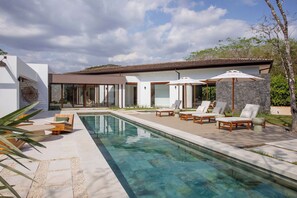 Ein modernes Haus mit Swimmingpool, Sitzgelegenheiten im Freien und einer Steinmauer.
