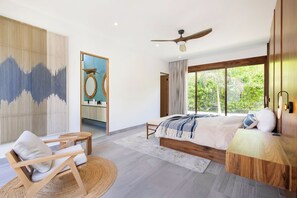 Un dormitorio moderno con una cama grande, un ventilador de techo y vistas a la vegetación exterior.