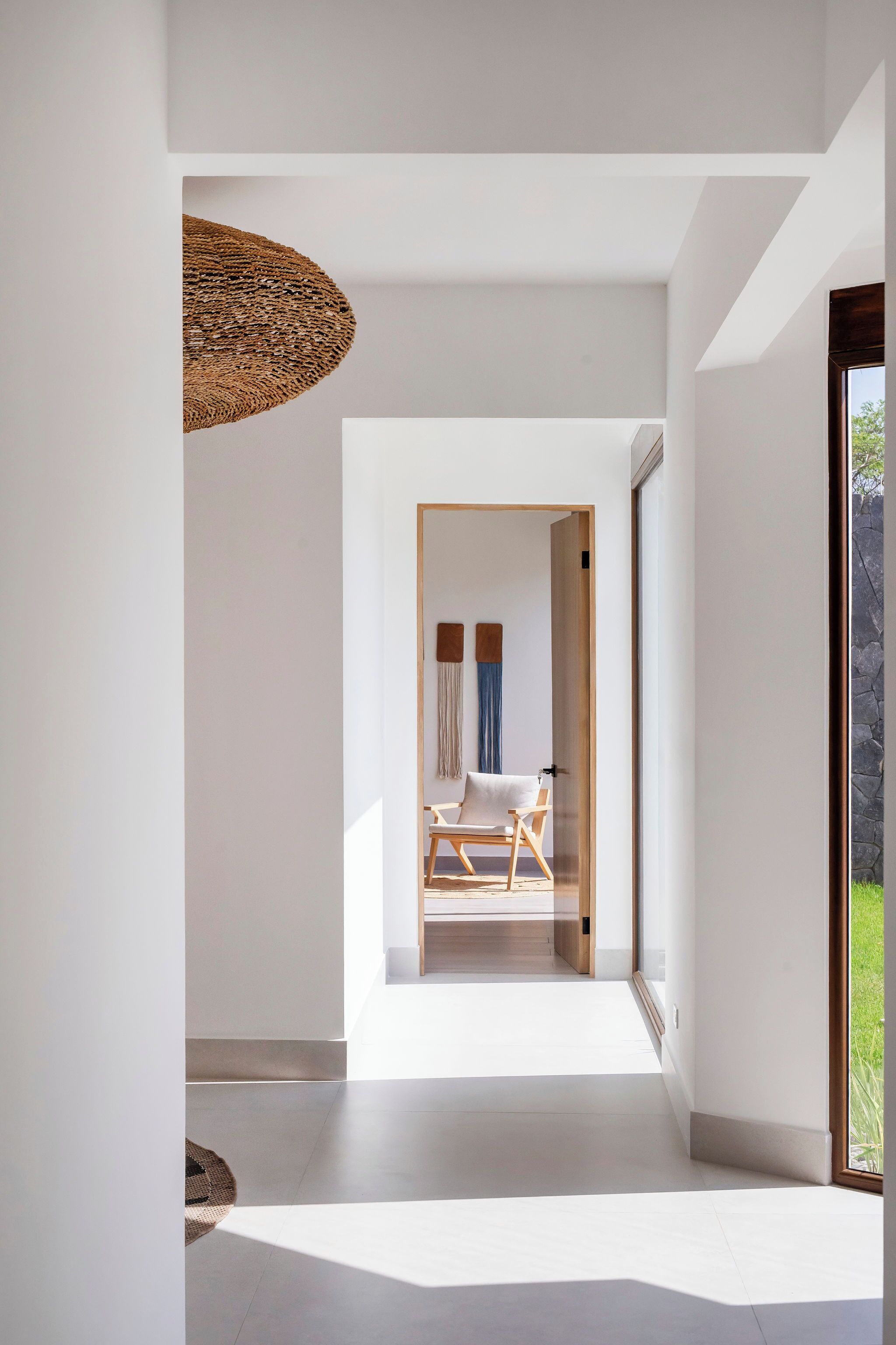 Un intérieur moderne au design minimaliste, avec un plancher en bois, un luminaire suspendu et une vue sur une pièce contenant un lit et des rideaux.