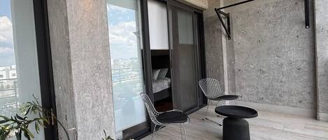 Un balcón con una cama, dos sillas, una mesa y plantas en macetas.