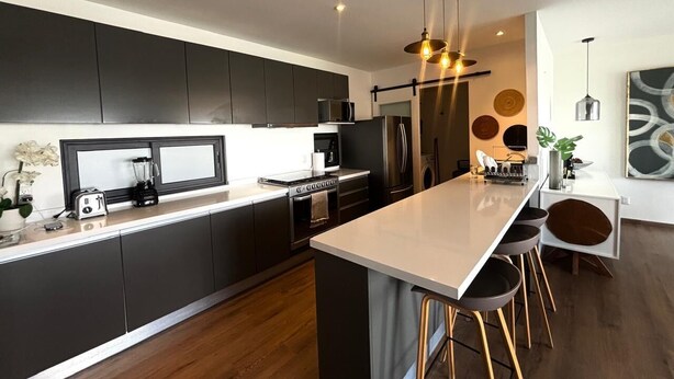 Een moderne keuken met donkere kastjes, een centraal eiland en barkrukken.
