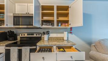 A compact kitchen with a microwave, stove, and open cabinets containing various kitchen items.