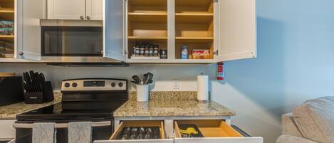 A compact kitchen with a microwave, stove, and open cabinets containing various kitchen items.