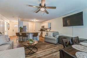 A modern living space with a dining area, kitchen, and a ceiling fan.