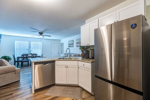 Une cuisine moderne dotée d’appareils électroménagers en acier inoxydable, de meubles blancs et d’un coin repas agrémenté d’un ventilateur de plafond.