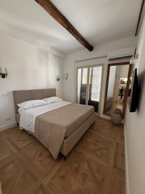 Ein Schlafzimmer mit einem Bett, Holzboden, weißen Wänden und einer Decke mit freiliegenden Balken.