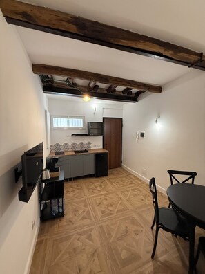Uma cozinha compacta com forno embutido, pia e piso de madeira. Há uma área de refeições com mesa e cadeiras.