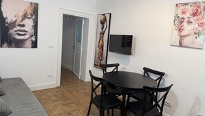 Um quarto com mesa de jantar, cadeiras, um sofá cinza e obras de arte nas paredes.