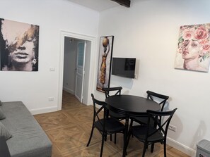 Ein Zimmer mit Esstisch, Stühlen, einer grauen Couch und Kunstwerken an den Wänden.
