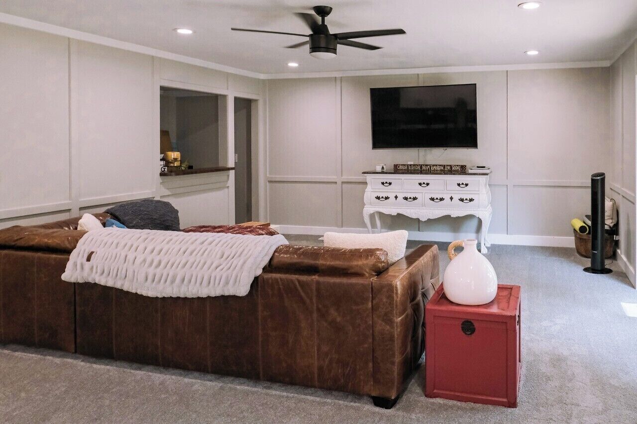 A living room with a brown leather sofa, a white entertainment unit, a flat-screen TV, and a ceiling fan.