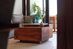Uma sala de estar moderna com uma mesa de centro de madeira, um sofá com almofadas e um vaso de planta.
