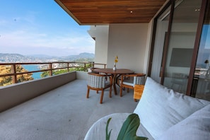 Un balcone con tavolo e sedie in legno, un divano e vista sul paesaggio costiero.