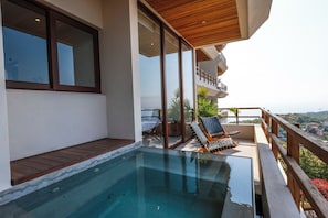 Ein moderner Außenpool mit Holzterrasse, Glasgeländer und Blick auf die Landschaft.