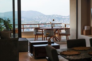Un balcone con tavolo e sedie in legno, una pianta in vaso e vista sulla città e sulle montagne.