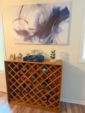 Un porte-bouteilles en bois contenant des bouteilles, un ensemble de verres et un objet décoratif posé sur le dessus.