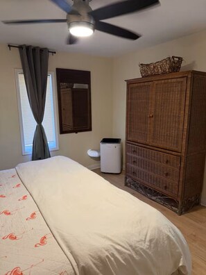 Ein Schlafzimmer mit einem Bett, einem Deckenventilator, einem Schminktisch und einem Fenster mit Vorhängen.