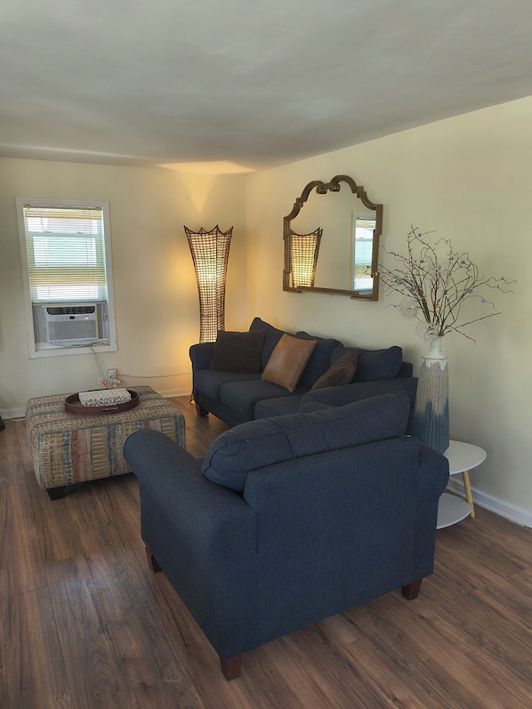 A living room with a sectional sofa, a patterned ottoman, a small side table, and a vase with branches.