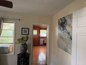 Ein Flur mit einer zur einem Zimmer führenden Tür, einem gerahmten Bild an der Wand und einem großen abstrakten Gemälde.