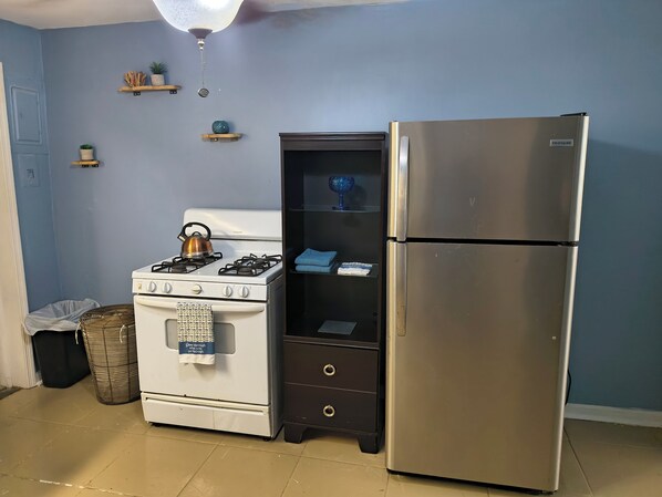 A compact kitchen with a white stove, a stainless steel refrigerator, and a small cabinet with glass doors.