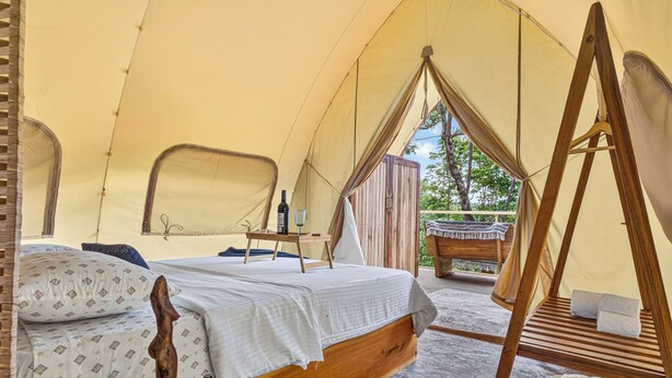 Una tenda amb un llit, una taula de fusta i una cadira penjant.
