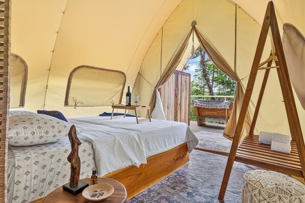 A tent with a bed, a wooden table, and a hanging chair.