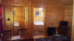 A wooden cabin with two beds, a television, and a small table with a book. - American Pines Cabin #5 (Keystone)