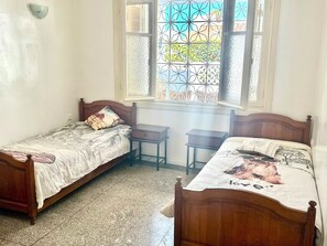 A bedroom with two wooden beds, a window with decorative metal bars, and a tiled floor. - Family villa with no neighbors directly across the street, 5 minutes from the beach - Sidi Bouzid (Sidi Bouzid)