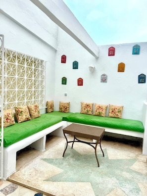 A white-walled room with a green sofa set, a woven table, and decorative wall hangings.