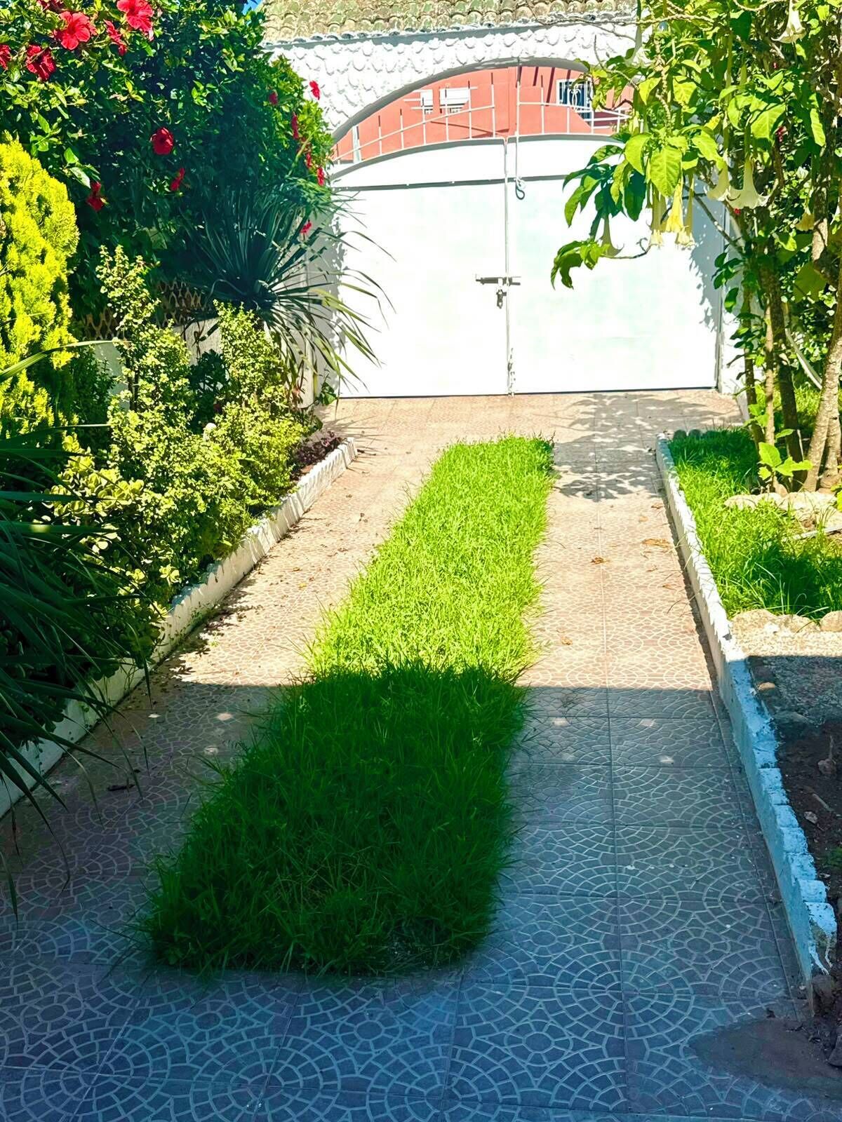 A pathway leading to a gated entrance with a tiled floor and a small grassy area.