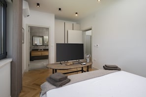 A modern hotel room with a large bed, a flat-screen TV, a wooden table, and a bathroom visible through an open door. - Villa BB near Rovinj (Bale)
