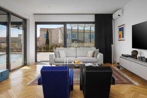 A modern living room with a sofa, coffee table, and chairs, a flat-screen TV, and a view of a pool and buildings. - Villa BB near Rovinj (Bale)