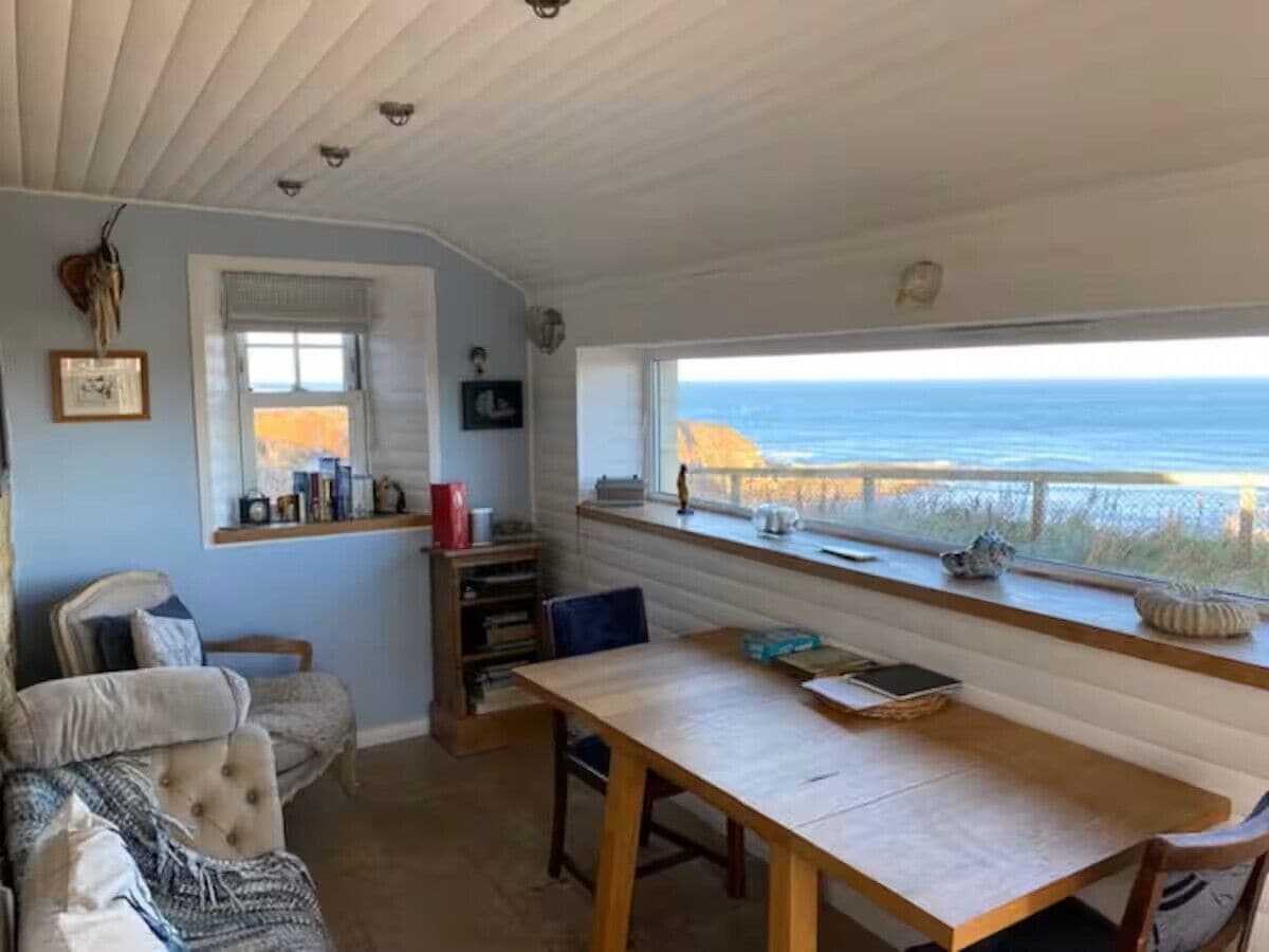 Una habitación con vista al océano, una mesa de madera, un sillón con cojines y una estantería.