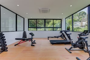 Une salle de sport moderne, équipée de matériel d’exercice, dotée de grandes fenêtres et offrant une vue sur la verdure.