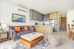 Ein modernes Wohnzimmer mit grauem Sofa, weißem Couchtisch und einem Essbereich mit Holzstühlen und einem kleinen Tisch.