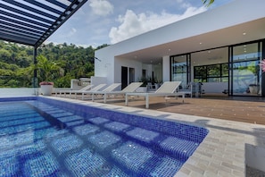 Un espace piscine extérieur moderne, doté de chaises longues et d’une terrasse offrant une vue sur un paysage verdoyant luxuriant.