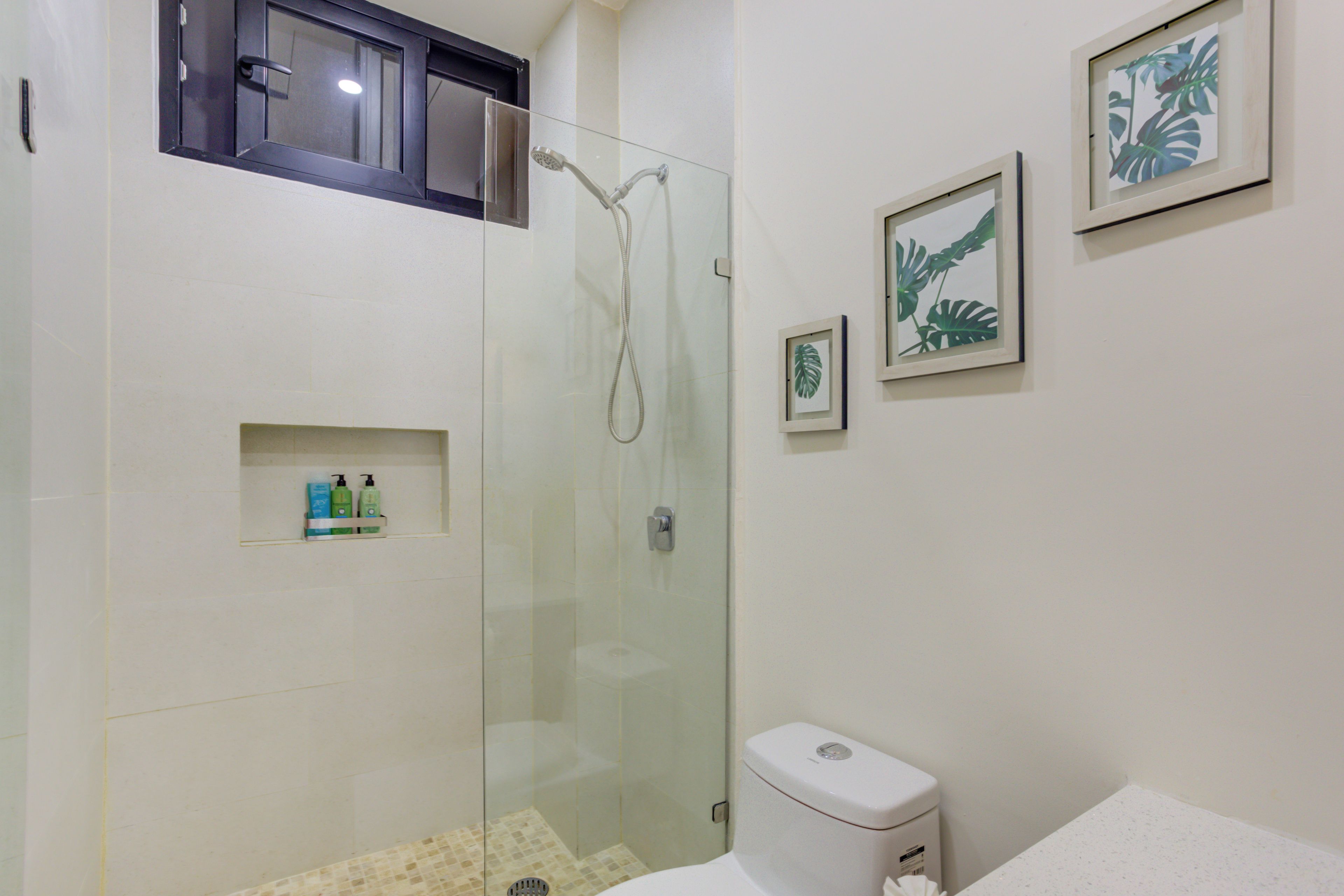 A bathroom with a glass-enclosed shower, a toilet, and framed botanical prints on the wall.