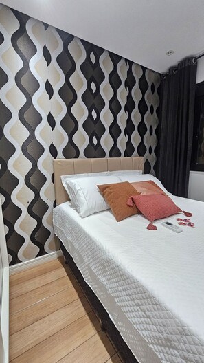 Quarto de hotel com parede estampada, cama com roupa de cama branca e chão de madeira.