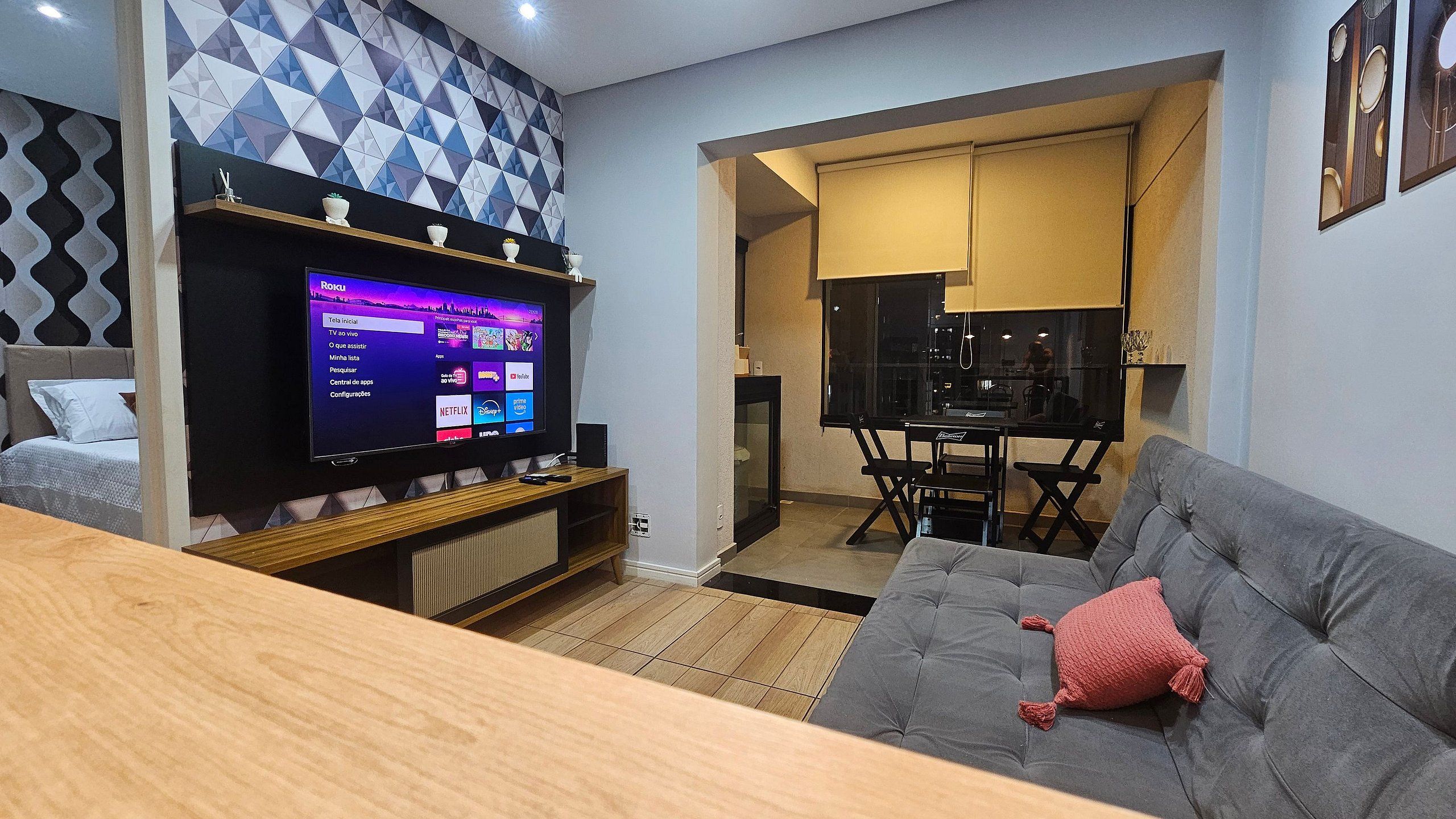 Uma sala de estar moderna com televisão de tela plana, sofá cinza, mesa de centro de madeira e parede com padrão.