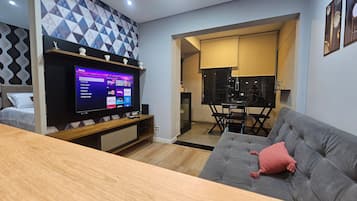 Uma sala de estar moderna com televisão de tela plana, sofá cinza, mesa de centro de madeira e parede com padrão.
