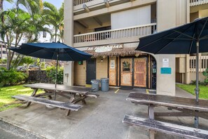 An outdoor dining area with picnic tables and umbrellas, a building with a sign reading "DA POKE SHACK," and a "NO Smoking" sign. - Banyan's Bungalow at The Kona Bali Kai (Kailua-Kona)