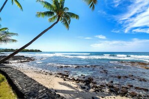 Ein Strand mit felsigem Ufer, Palmen und Wellen.