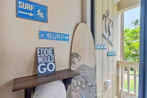 A room with a surfboard leaning against the wall, a surfboard on a shelf, and a sign that says 'EDDIE WOULD GO'. - Banyan's Bungalow at The Kona Bali Kai (Kailua-Kona)
