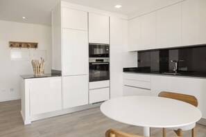 A modern kitchen with white cabinetry, a Bosch oven, and a round dining table with chairs. - Skyline Consolação Flat - Shared Rooftop Pool (Peniche)