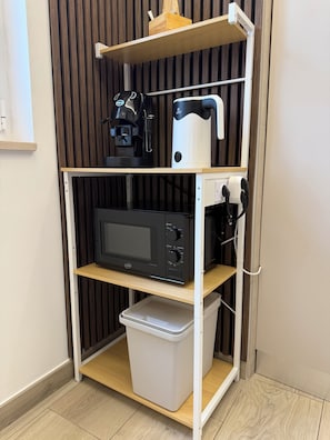 Eine Küchenzeile mit Mikrowelle, Kaffeemaschine und einem Mülleimer auf einer weißen Schrankwand.