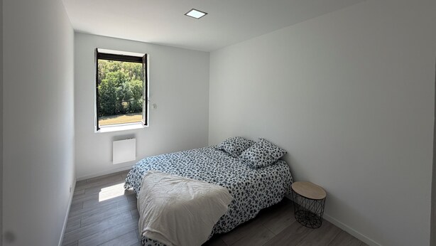 Een slaapkamer met een bed, nachtkastje, raam en radiator.