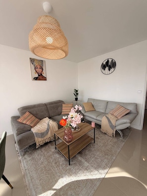 A modern living room with a grey sofa, a wooden coffee table with a vase of flowers, a woven pendant light, and a wall art piece. - Ecrin de Villiers, between Paris Disney and Accor Arena (Villiers-sur-Marne)