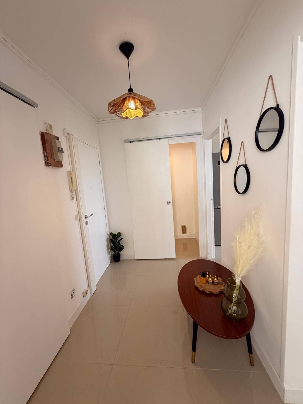 A hallway with a round wooden table, a hanging pendant light, and a potted plant.
