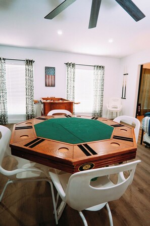 Ein Zimmer mit einem großen achteckigen Tisch, weißen Stühlen, einem Holzschrank und einem Deckenventilator.